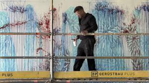 Imran Qureshi mit Pinsel Größe 14 und einem Becher mit Farbe, den er immer wieder an der Wand ausgießt. F