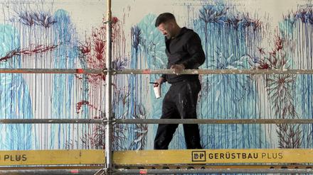 Imran Qureshi mit Pinsel Größe 14 und einem Becher mit Farbe, den er immer wieder an der Wand ausgießt. F