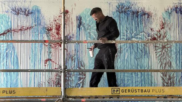 Imran Qureshi mit Pinsel Größe 14 und einem Becher mit Farbe, den er immer wieder an der Wand ausgießt. F