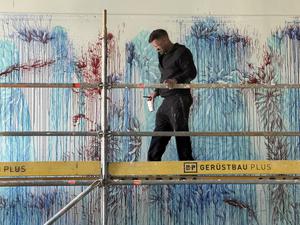 Imran Qureshi mit Pinsel Größe 14 und einem Becher mit Farbe, den er immer wieder an der Wand ausgießt. F