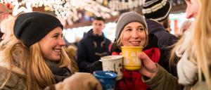 Freunde wärmen sich mit Glühwein auf einem Weihnachtsmarkt auf.