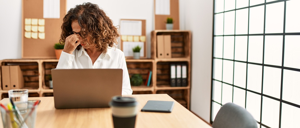 Middle age hispanic woman working at the office wearing glasses tired rubbing nose and eyes feeling fatigue and headache. stress and frustration concept.