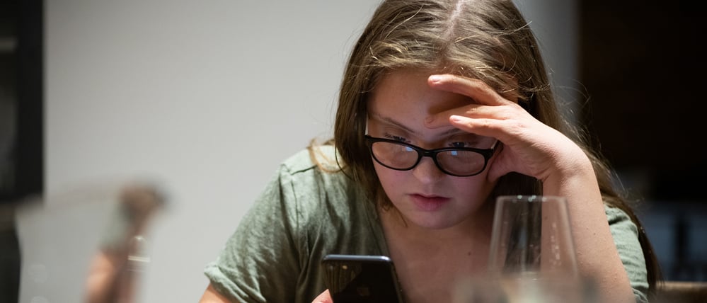 Eine junge Frau mit Downsyndrom schaut auf ihr Smartphone (Symbolbild).