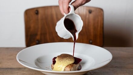 Eine Hand gieße dunkle Sauce über ein Gericht.