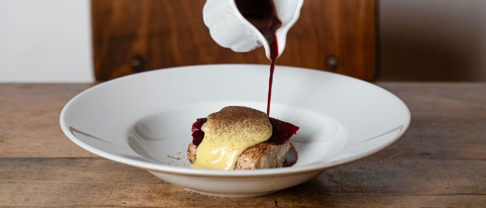 Eine Hand gieße dunkle Sauce über ein Gericht.