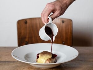 Eine Hand gieße dunkle Sauce über ein Gericht.