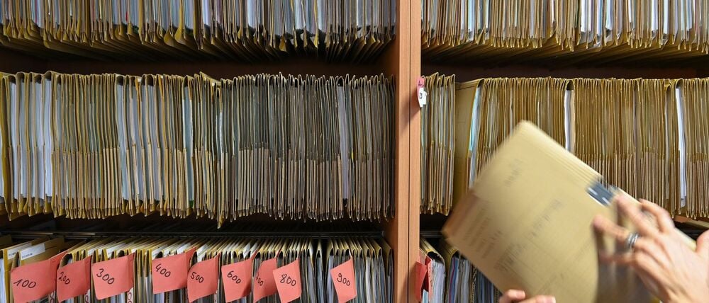 Deutsche Gegenwart: Eine Mitarbeiterin einer Behörde greift an einem Regal nach einer Akte. 