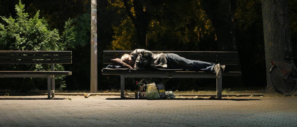 Ein Obdachloser hat sich zum Schlafen auf eine Bank gelegt (Symbolbild). 