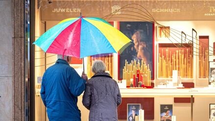 Zwei ältere Personen stehen bei Regen vor einem Schaufenster eines Schmuckgeschäfts und betrachten die ausgestellten Waren (Symbolbild).