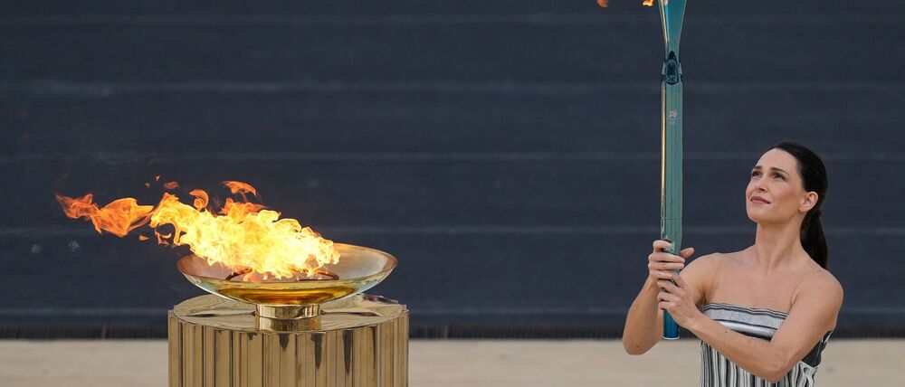 Schauspielerin Mary Mina, in der Rolle der Hohepriesterin, entzündet eine Fackel bei der Zeremonie zur Übergabe der Flamme der Olympischen Winterspiele 2026 im Panathinaikon-Stadion.