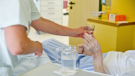 Eine Krankenpflegerin reicht einem Patienten ein Glas Wasser.