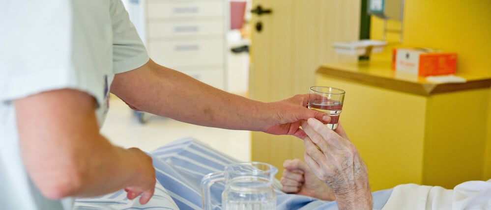 Eine Krankenpflegerin reicht einem Patienten ein Glas Wasser.
