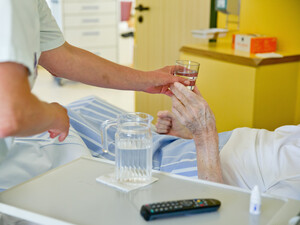 Eine Krankenpflegerin reicht einem Patienten ein Glas Wasser.