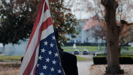 Ein Mann mit einer auf dem Kopf stehenden Flagge steht am 4. Dezember 2025 vor dem Weißen Haus in Washington, D.C., USA.