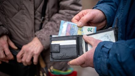 Eine ältere Person hält im öffentlichen Raum eine geöffnete Geldbörse in der Hand.