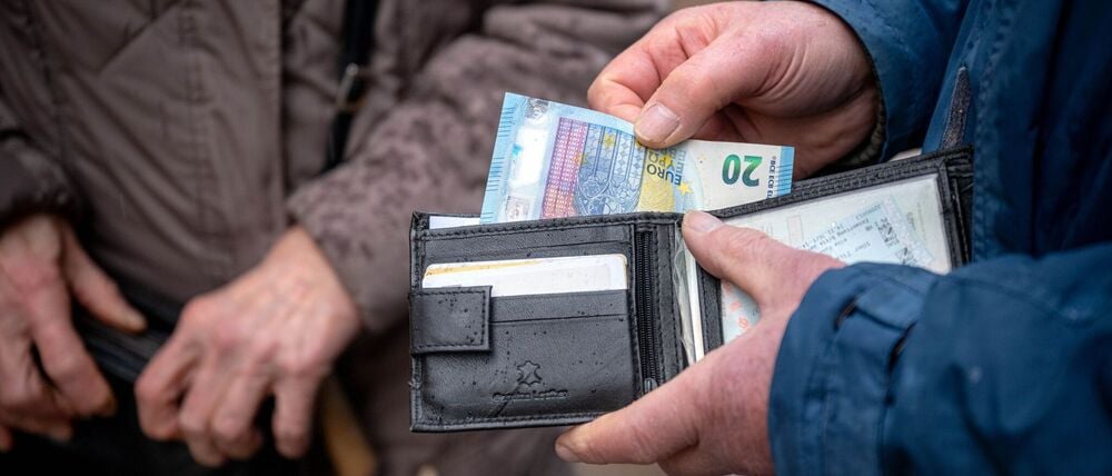 Eine ältere Person hält im öffentlichen Raum eine geöffnete Geldbörse in der Hand.