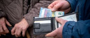 Eine ältere Person hält im öffentlichen Raum eine geöffnete Geldbörse in der Hand.