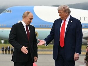 US-Präsident Donald Trump (rechts) streckt seine Hand aus, um dem russischen Präsidenten Wladimir Putin die Hand zu schütteln, während sie nach ihrer Ankunft auf der Joint Base Elmendorf-Richardson in Anchorage, Alaska, am 15. August 2025 auf einem Podium auf dem Rollfeld posieren. 