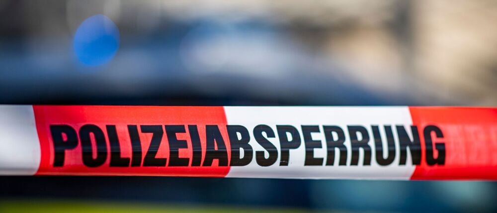 Ein Absperrband mit der Aufschrift „Polizeiabsperrung“ ist vor einem Polizeiwagen aufgespannt.