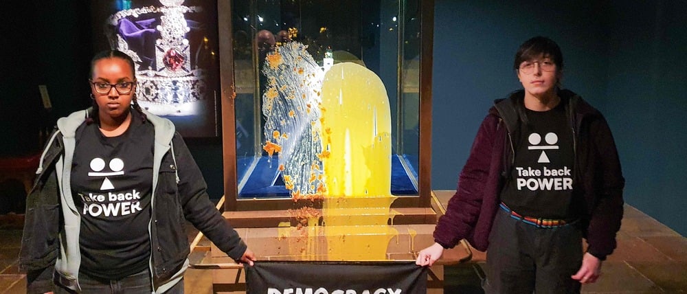 Das Bild zeigt Anhänger der zivilen Widerstandsgruppe „Take Back Power“ mit einem Banner mit der Aufschrift „Democracy has crumbled – Tax The Rich” (Die Demokratie ist zusammengebrochen – Besteuert die Reichen).