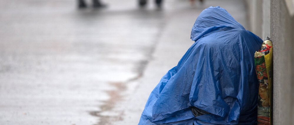 ARCHIV - 23.03.2018, Brandenburg, Potsdam: Ein Bettler sitzt mit einem Regenumhang am Rande eines Gehweges. (zu dpa: ´Weniger Straftaten gegen Obdachlose in Brandenburg») Foto: Ralf Hirschberger/dpa +++ dpa-Bildfunk +++
