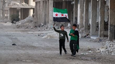 Zwei Jungen gehen mit syrischen Flaggen durch eine Straße im kriegszerstörten Damaskus-Vorort Daraya.