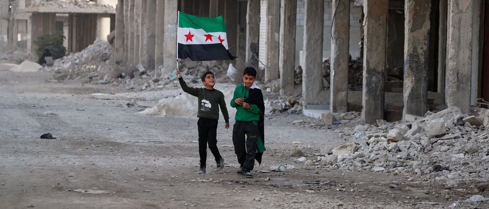 Zwei Jungen gehen mit syrischen Flaggen durch eine Straße im kriegszerstörten Damaskus-Vorort Daraya.