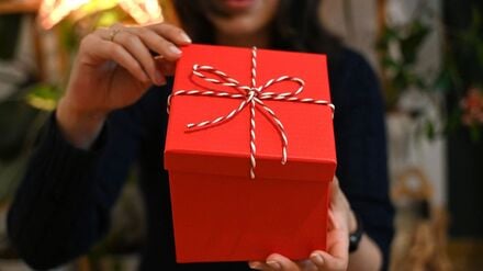 Eine Frau öffnet eine mit einer Schleife verzierte Geschenkbox. An Weihnachten legt sich rund ein Viertel der Bundesbürger inzwischen auch ein Geschenk für sich selbst auf den Gabentisch.