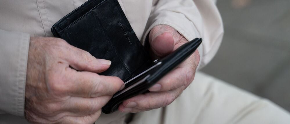 Ein Rentner hält sein Portemonnaie in der Hand.