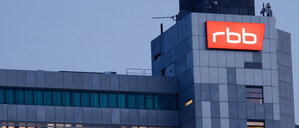 Das beleuchtete Logo des Senders Rundfunk Berlin-Brandenburg (RBB) ist an der Fassade am Sitz des Senders an der Masurenallee angebracht.
