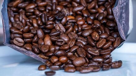 Geröstete Kaffeebohnen liegen vor einer Tüte (Symbolbild).