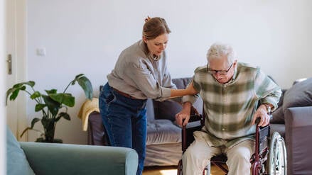 Eine Frau hilft in einer Wohnung einem Mann im Rollstuhl (Symbolfoto).