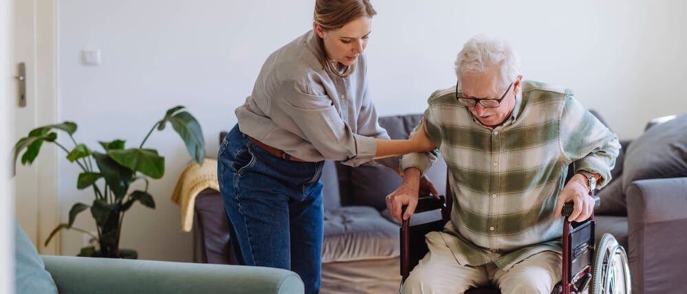 Eine Frau hilft in einer Wohnung einem Mann im Rollstuhl (Symbolfoto).