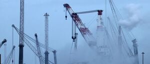 Im Überseehafen an der Ostsee steigt am Morgen Dampf aus Anlagen am Getreideterminal auf, im Hintergrund stehen neue mobile Hafenkräne des Kranwerks Liebherr-MCCtec Rostock. 