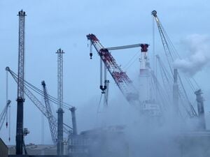 Im Überseehafen an der Ostsee steigt am Morgen Dampf aus Anlagen am Getreideterminal auf, im Hintergrund stehen neue mobile Hafenkräne des Kranwerks Liebherr-MCCtec Rostock.