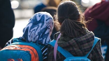 Ein Mädchen mit Kopftuch steht neben einem Mädchen ohne Kopfbeckedung.