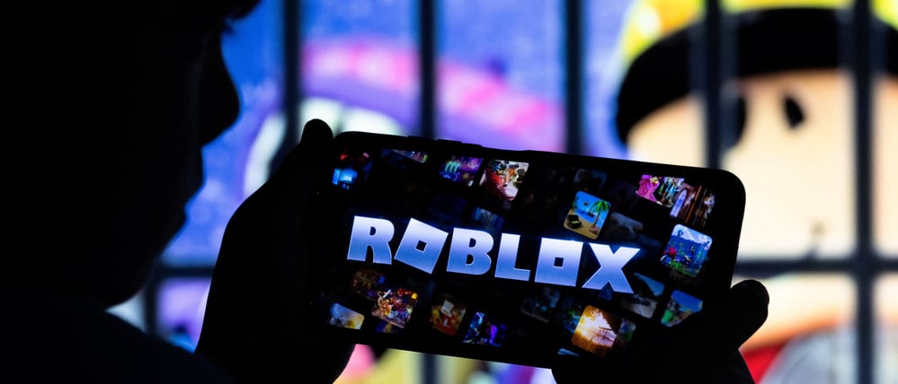 Ein Junge posiert für ein Foto, während er ein Gamepad vor einem Bildschirm hält, auf dem das Logo der US-amerikanischen Gaming-Plattform Roblox zu sehen ist. Diese Illustration stammt vom 8. Dezember 2025.