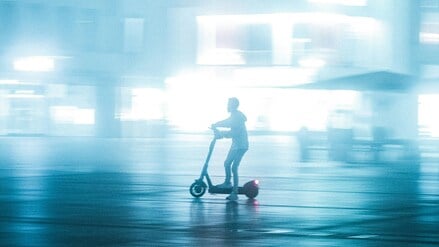 Eine Person fährt nachts auf einem E-Scooter durch die Stadt.