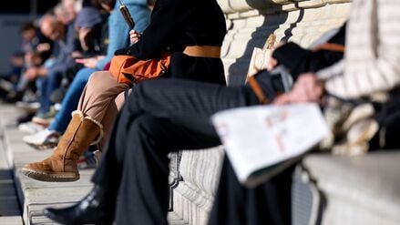 Menschen sitzen am Max-Joseph-Platz in München auf einer Bank in der Sonne.