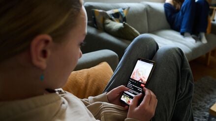 Ein Mädchen nutzt ihr Smartphone, während ein anderes Mädchen ein Buch liest. (gestellte Szene)