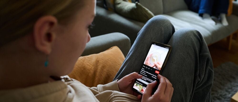 Ein Mädchen nutzt ihr Smartphone, während ein anderes Mädchen ein Buch liest. (gestellte Szene)