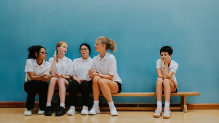 Vier Mädchen auf einer Bank in einer Sporthalle grenzen ein weiteres Mädchen aus (Symbolbild).