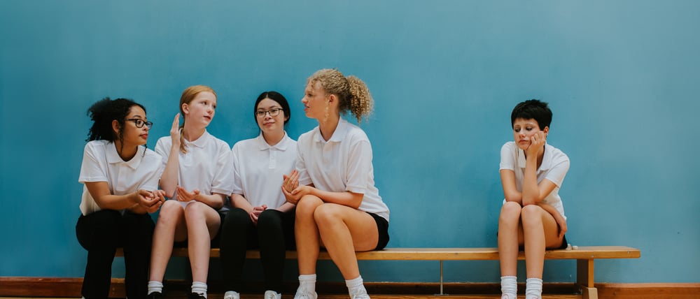 Vier Mädchen auf einer Bank in einer Sporthalle grenzen ein weiteres Mädchen aus (Symbolbild).