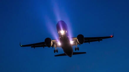 Ein Passagierflugzeug ist am Abend mit bereits ausgefahrenem Fahrwerk und Scheinwerferlicht im Landeanflug auf den BER Hauptstadtflughafen.
