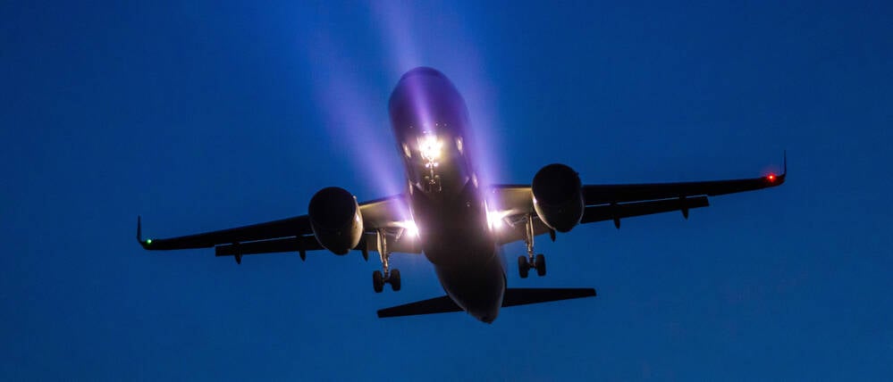 Ein Passagierflugzeug ist am Abend mit bereits ausgefahrenem Fahrwerk und Scheinwerferlicht im Landeanflug auf den BER Hauptstadtflughafen.
