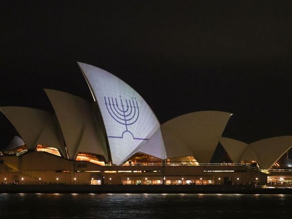 A Hanukkah menorah is projected onto the sails of the Sydney Opera House in memory of the victims of a shooting at Bondi Beach, in Sydney on December 15, 2025. A father and son opened fire on a Jewish festival at Australia's Bondi Beach in a shooting spree that killed 15 people, including a child, authorities said on December 15, denouncing the attack as antisemitic "terrorism". (Photo by DAVID GRAY / AFP)