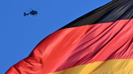Ein Hubschrauber fliegt über eine deutsche Flagge, die auf dem Gebäude des Reichstags weht.