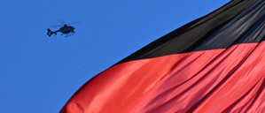 Ein Hubschrauber fliegt über eine deutsche Flagge, die auf dem Gebäude des Reichstags weht.