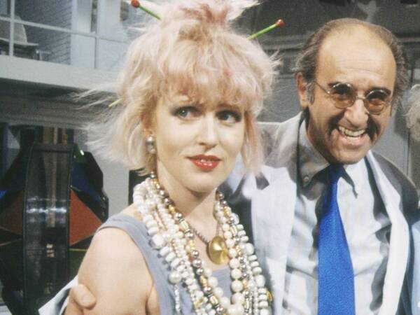 Alfred Biolek mit den Schwestern Annette li. und Inga Humpe in Mensch Meier 06/85 vZ Mann Moderator Moderation TV Fernsehen Brille dunkelhaarig kurzhaarig Halbglatze seriös Jackett Krawatte halb quer stehend TV-Studio Kulisse Dekoration Bühne lächelnd umarmend Schmuck Kette Ketten