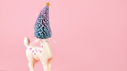 Pastel holiday scene with deer figure with Christmas tree head on pink background. Room for copy.